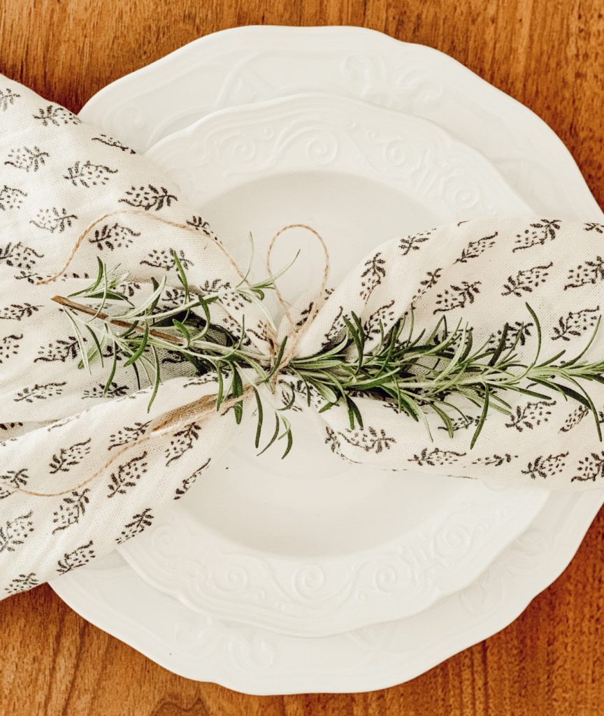 Summer tablescape with a napkin tied with fresh rosemary.