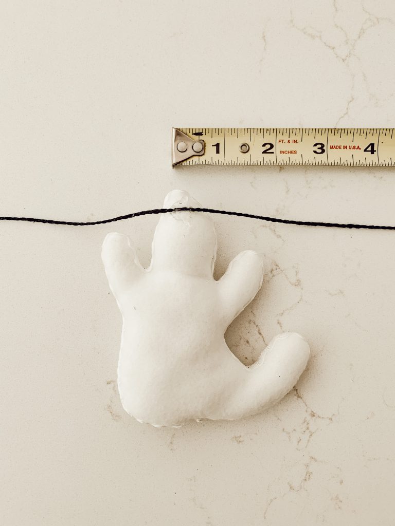Creating a ghost garland with ghosts, black yarn, and hot glue.