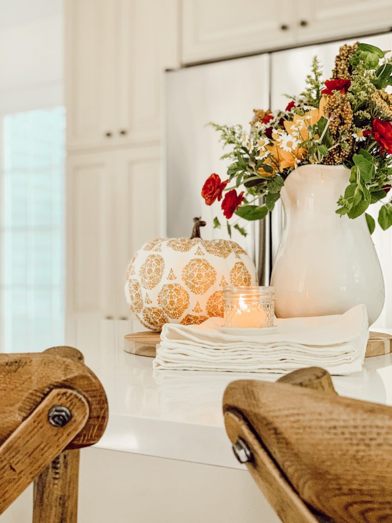 Decorative pumpkin on kitchen counter with pitcher of fresh flowers.