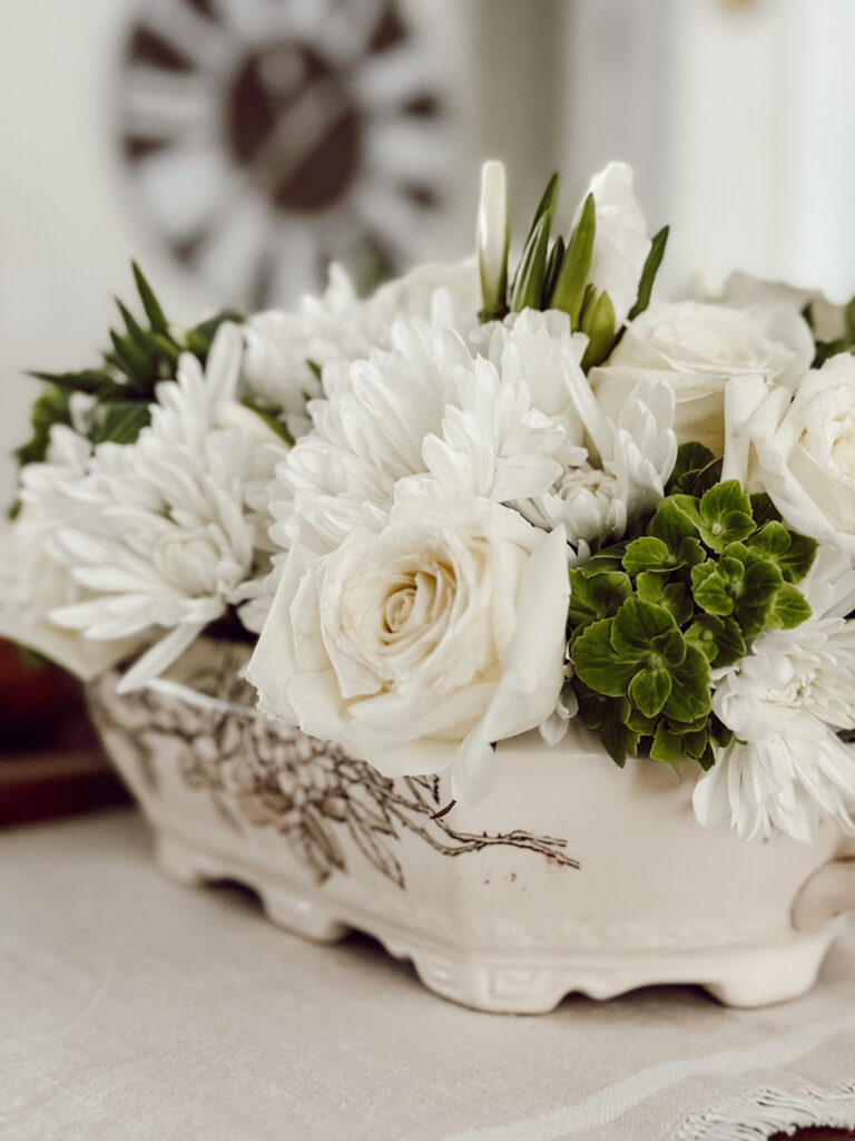 An arrangment on a tablescape using a soup tureen and flowers tucked inside the tureen.