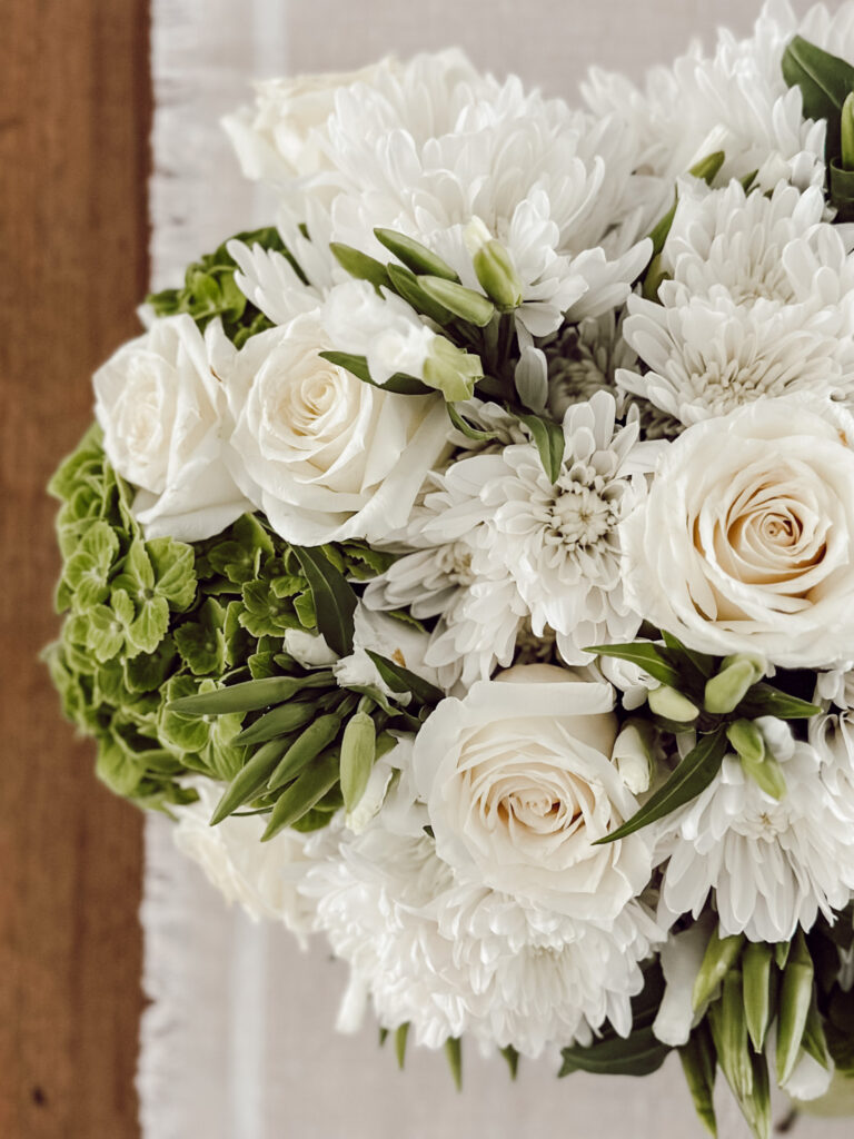 White and green flower arrangement in soup tureen on a wooden table.