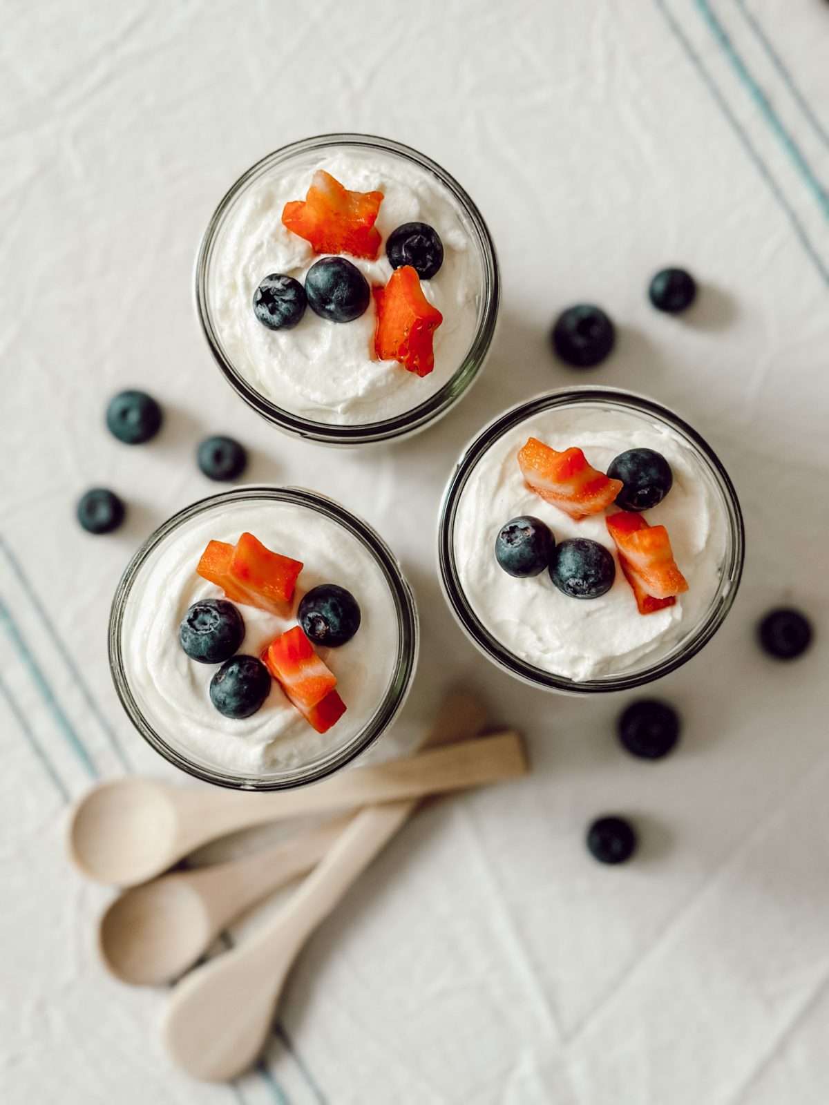 N-bake berry cheesecake trifles with fresh strawberries and blueberries packed in mason jars with mini wooden spoons for eating.