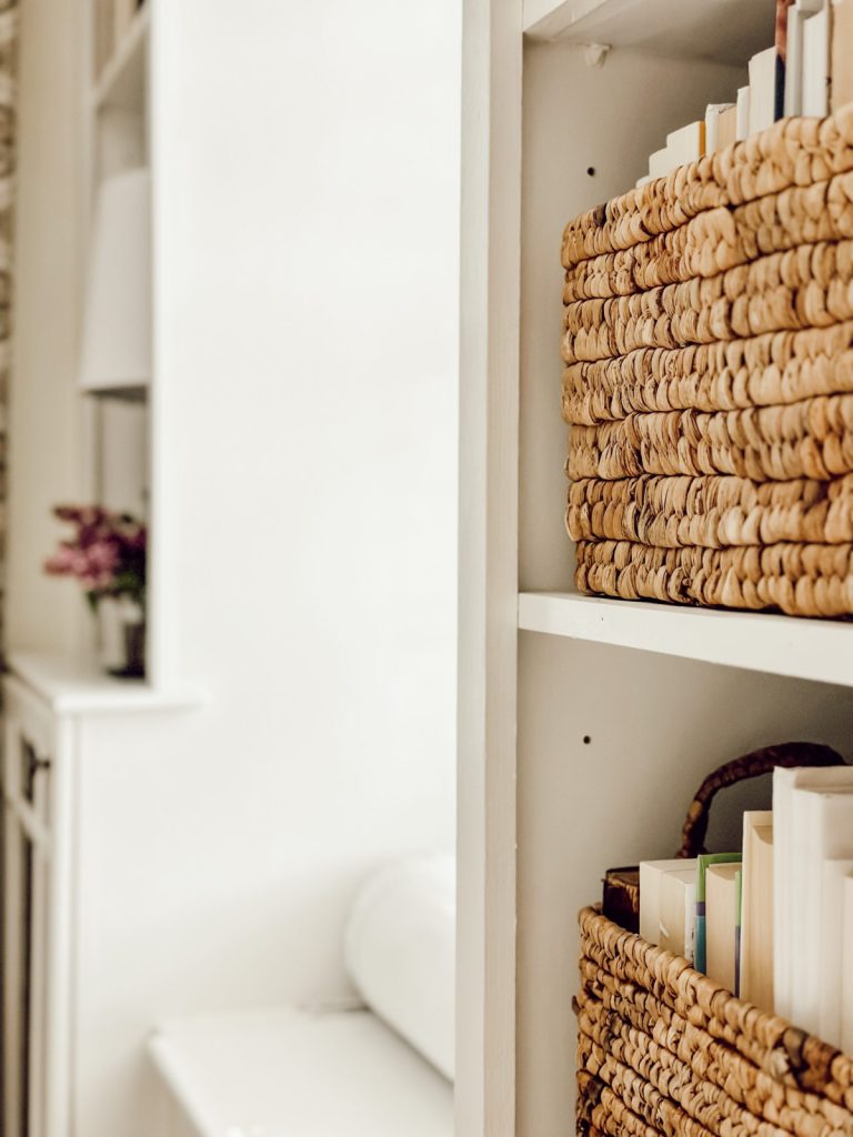 A cozy bookshelf decorated with wicker baskets and books.
