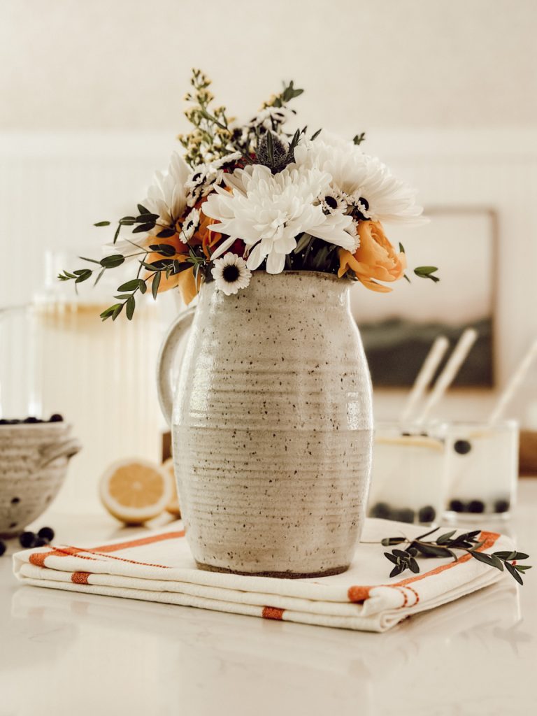 Summer pitcher filled with fresh flowers with glasses of lemonade on the side.