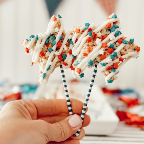 Heidi holding star shaped Rice Krispie treats on a stick drizzled with white chocolate.