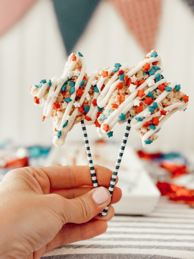 Heidi holding star shaped Rice Krispie treats on a stick drizzled with white chocolate.