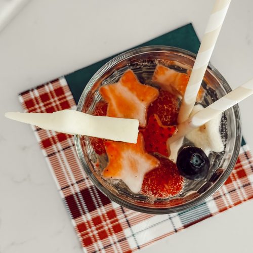 White wine sangria with vodka and berries in a glass cup with star shaped fruit on a red, white, and blue napkin.