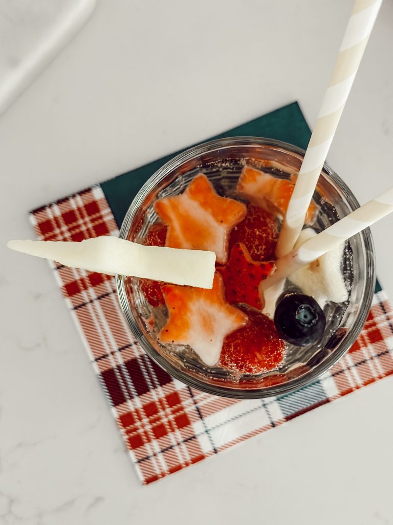 White wine sangria with vodka and berries in a glass cup with star shaped fruit on a red, white, and blue napkin.