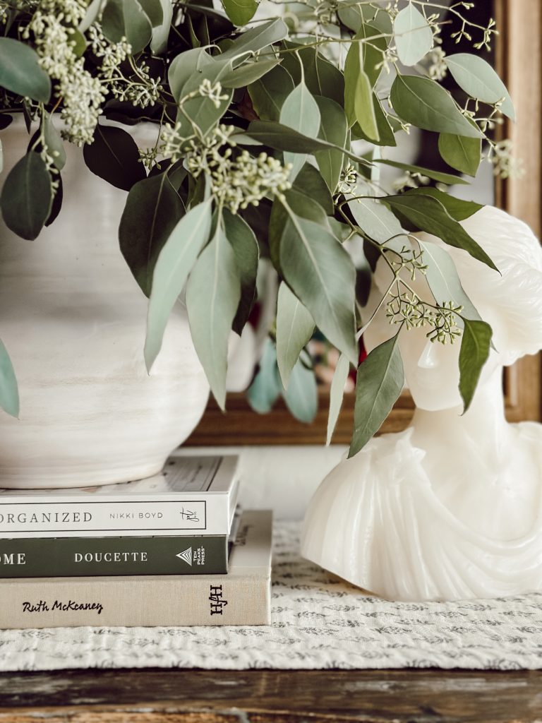 Neutral vase of seeded eucalyptus on a wooden dresser in the living room.