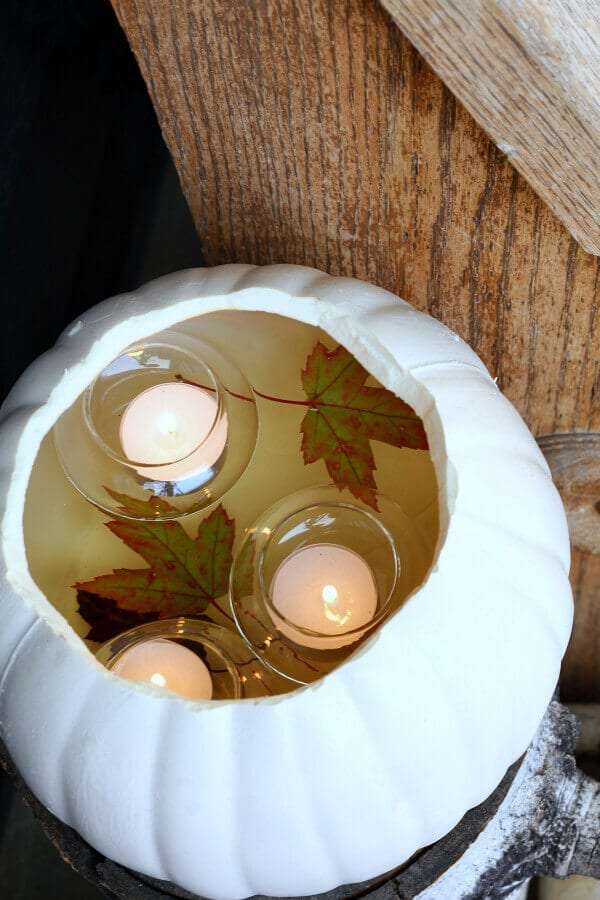 Floating votives in a faux pumpkin with water and leaves.