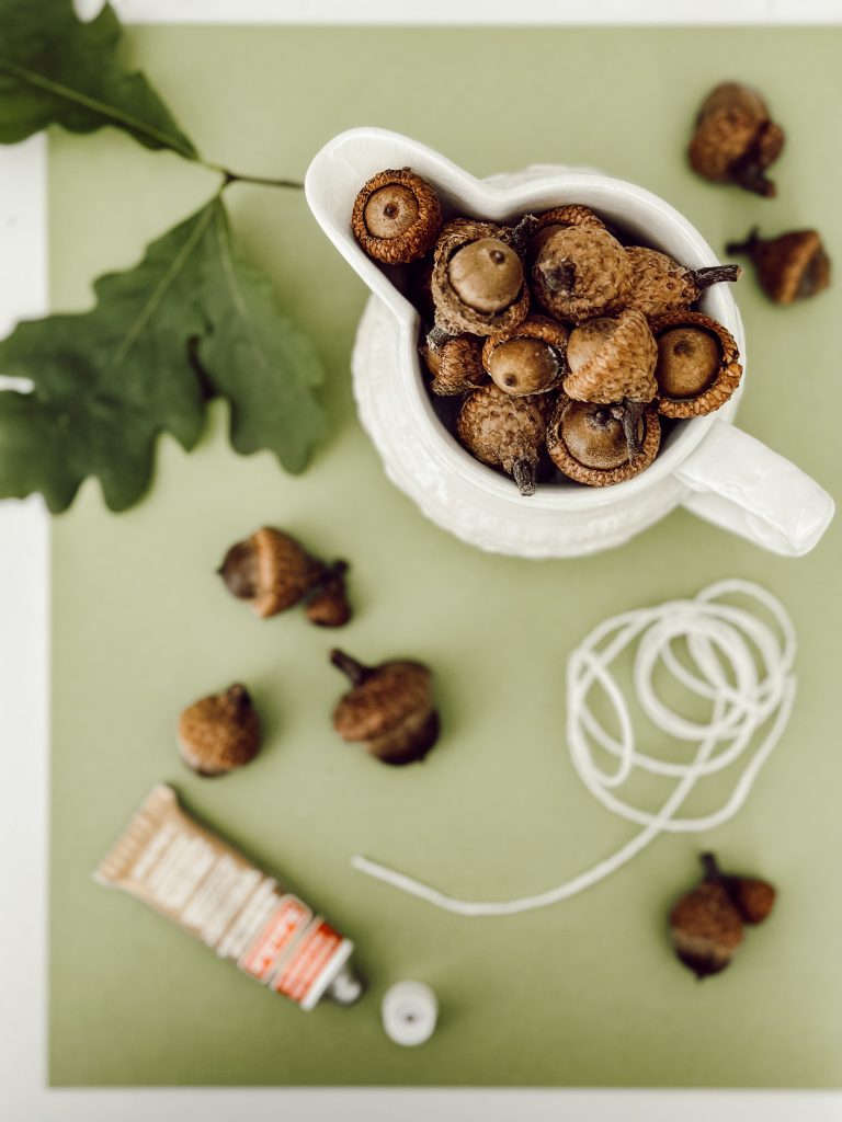 All the supplies you need for a DIY fall garland that include acorns, twine, and card stock.
