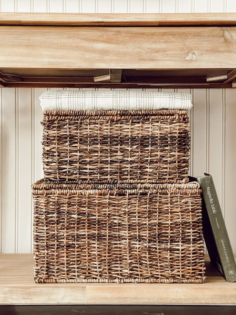 Stacked baskets in the kitchen with a patterned pretty tablecloth, and a cookbook.