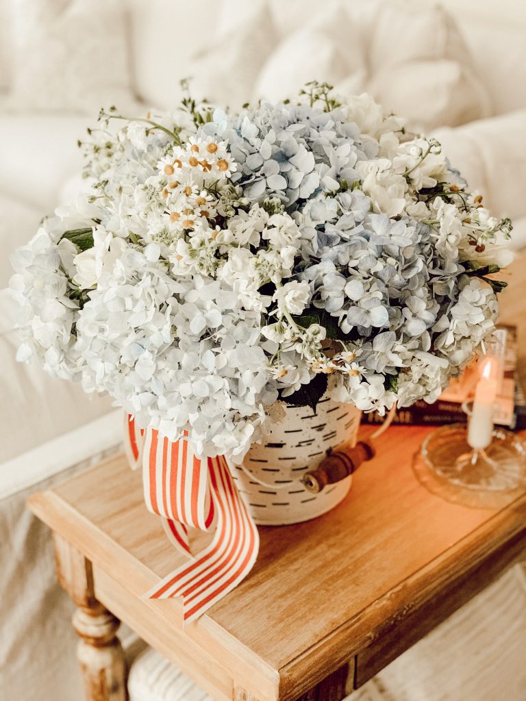 Blue flowers with chamomile in a vintage bucket with red striped ribbon for patriotic summer decor.