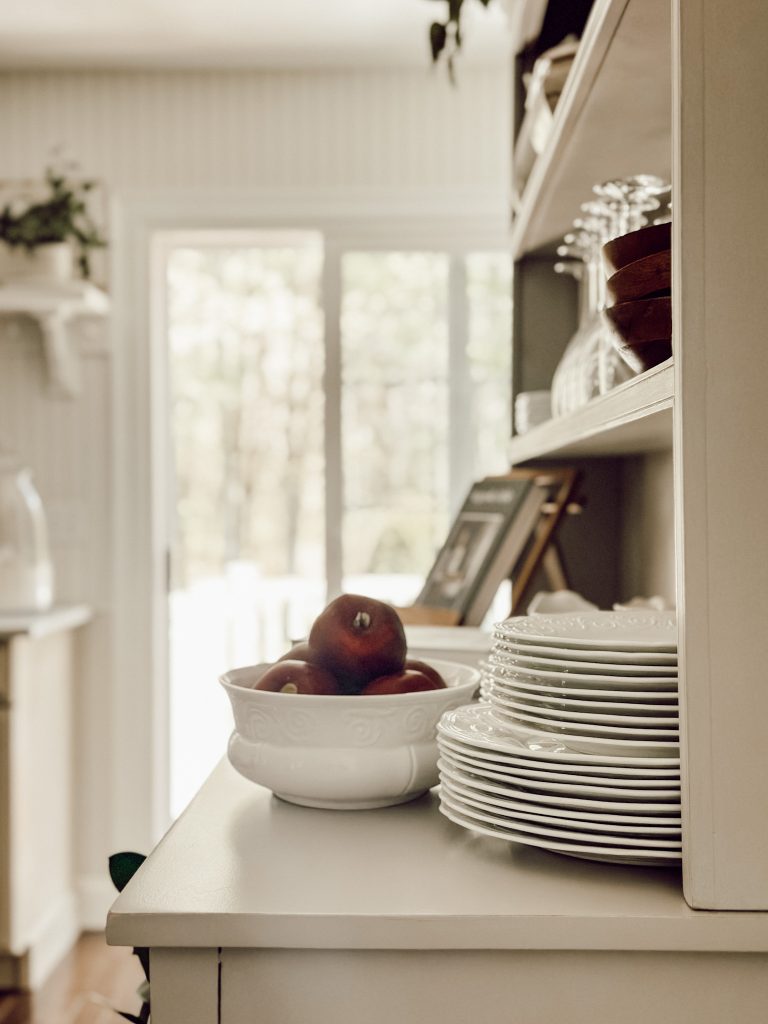Place different items on a china hutch in the kitchen like dishes, bowls, glasses, and decorative objects.