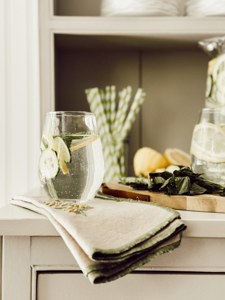 A healthy drink in a large pitcher with fresh lemons, cucumbers, mint and cold water.