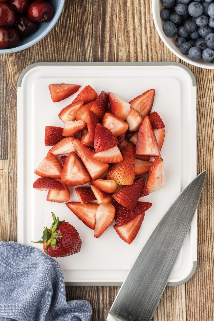 Fresh red strawberries cut into quarters for a patriotic fruit salad recipe.