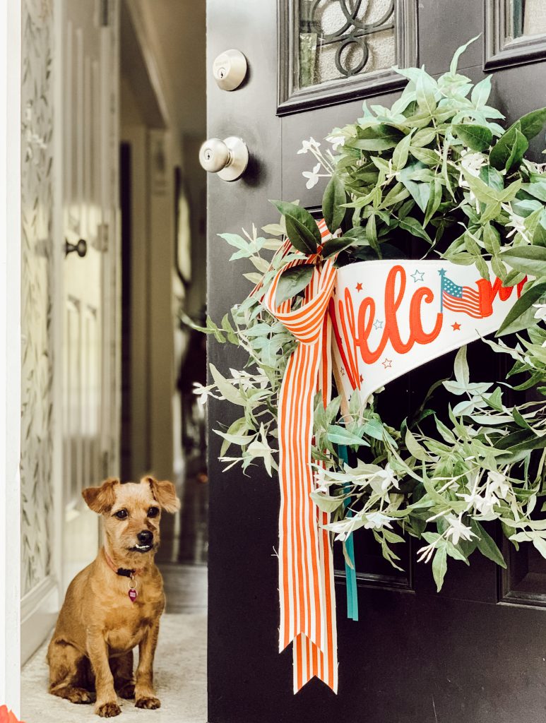 Wreath tied with red ribbon and a welcome banner for front door decorations.