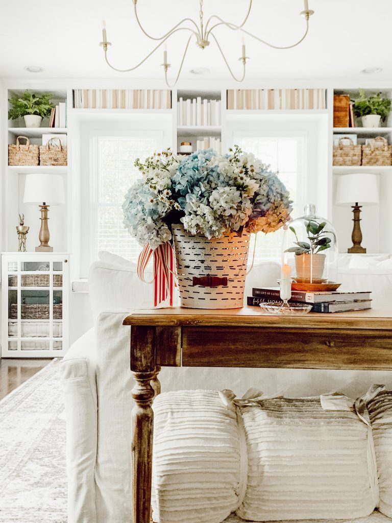 Living room 4th of July decor with a bucket of flowers and a candle.