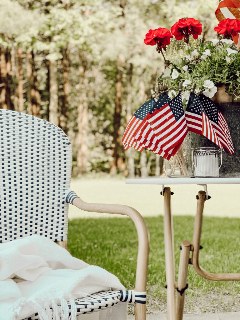 Decorate your outdoor space for 4th of July with miniature flags, red flowers, and blue Mason jars with candles.