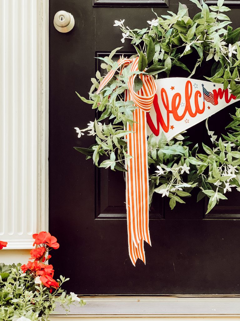 Patriotic front door decorations with a festive wreath and red flowers.
