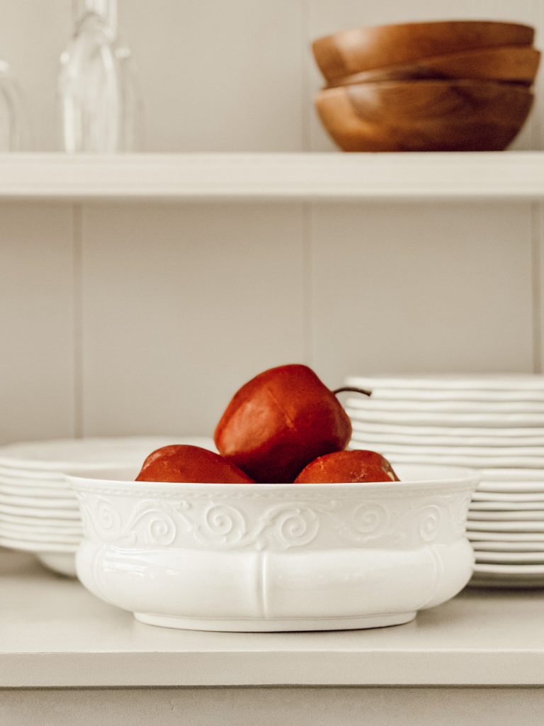 Red apples in a white stoneware bowl styled on the open shelf of our kitchen china hutch.