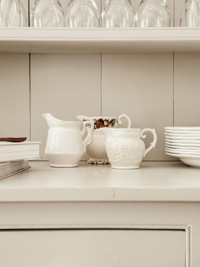 A group of three ironstone creams on shelf in kitchen hutch.