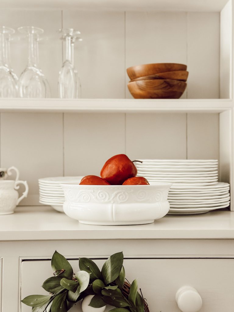 White ironstone dishes with salad plates, wooden bowls, and glassware in a china hutch. 