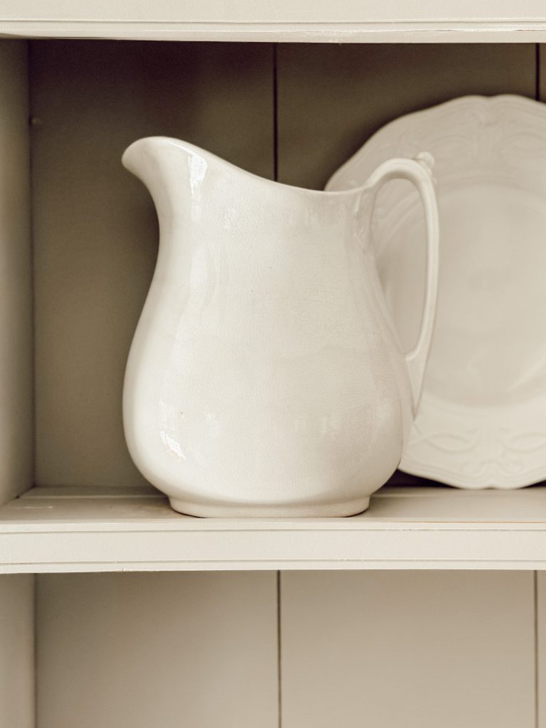 White ironstone pitcher on hutch shelf with a white platter for depth & dimension.
