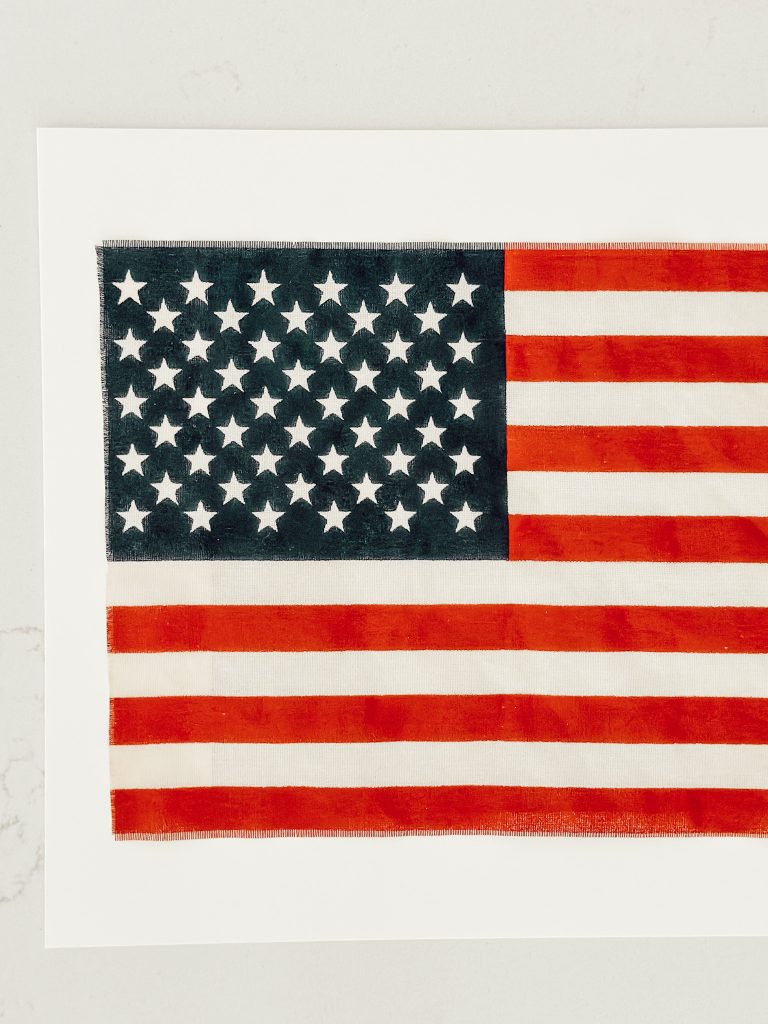 Use double sided fabric tape to attach the tea stained flag to the frame mat.