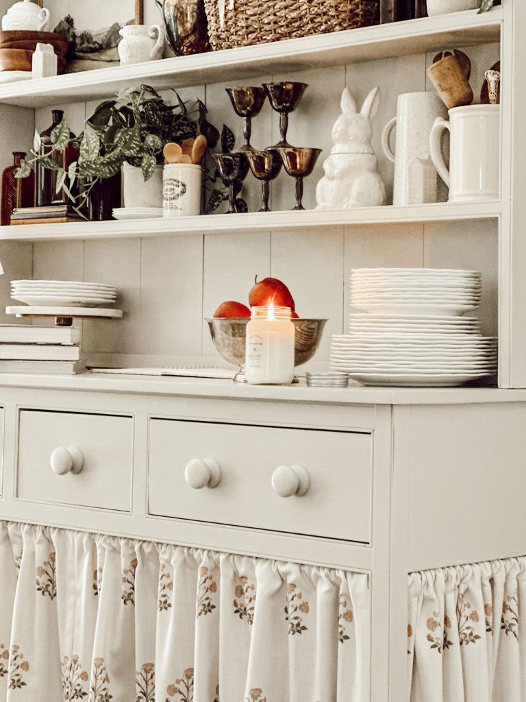Fall decorated kitchen hutch with a fall-scented candle and natural elements.