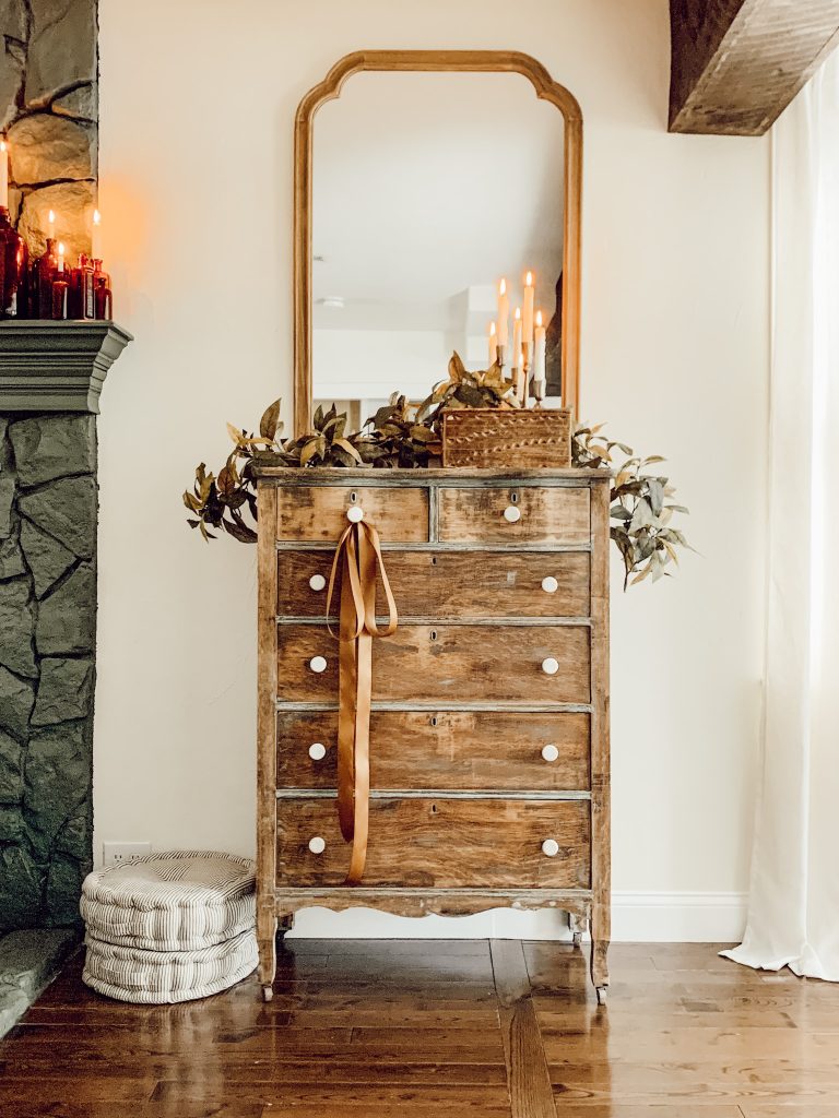 Vintage dresser decorated for autumn with candles, book, and brown ribbon.