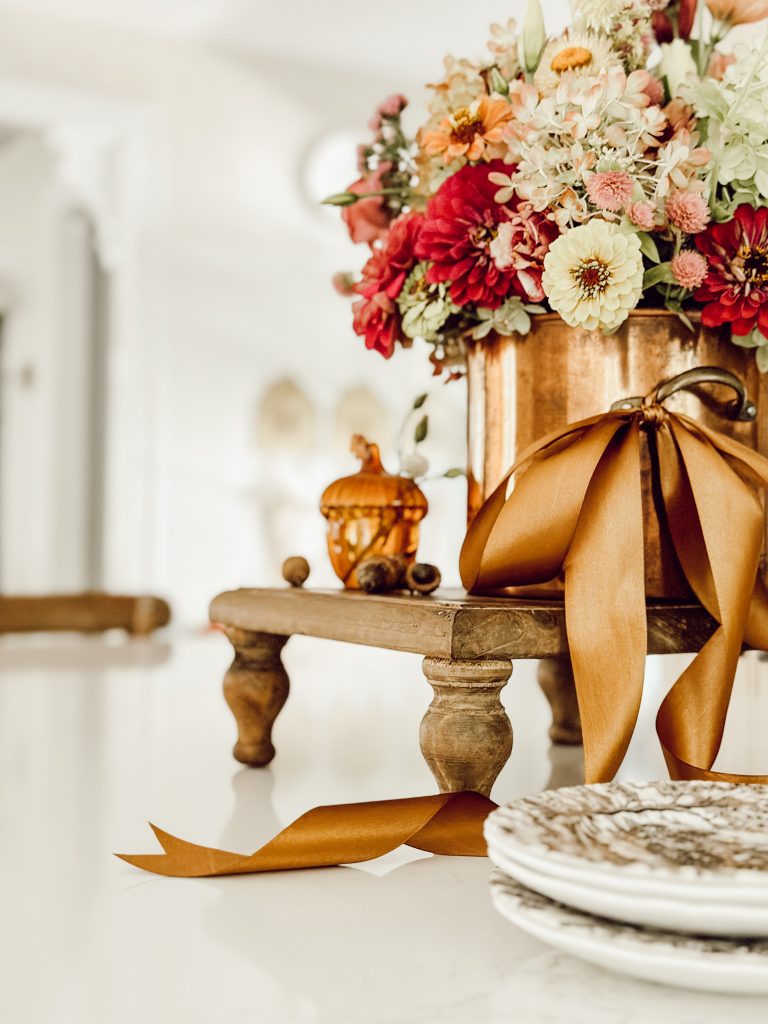 Create a Thanksgiving display with a copper pot, fresh flowers, and transfer ware plates.