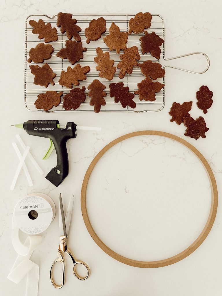 DIY fall wreath supplies include a wreath ring, hot glue gun, velvet ribbon, scissors, and salt dough leaves.
