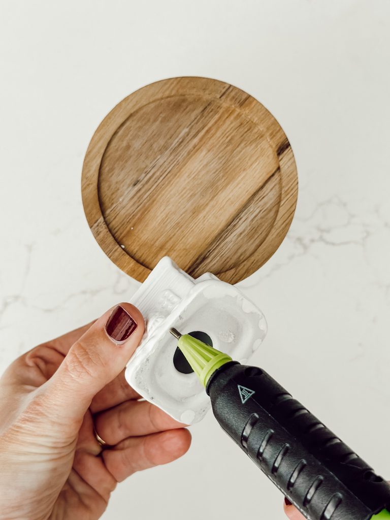 Using a hot glue gun to attach the house ornament to the top of the glass container.