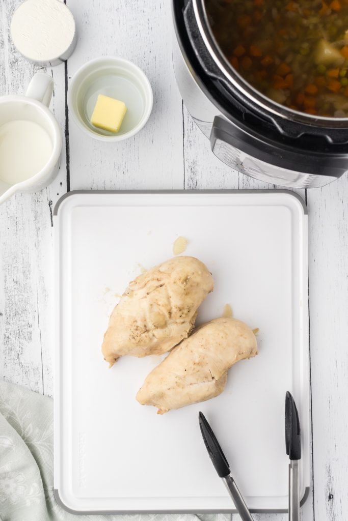 Juicy chicken breasts on a cutting board for traditional chicken pot pie.