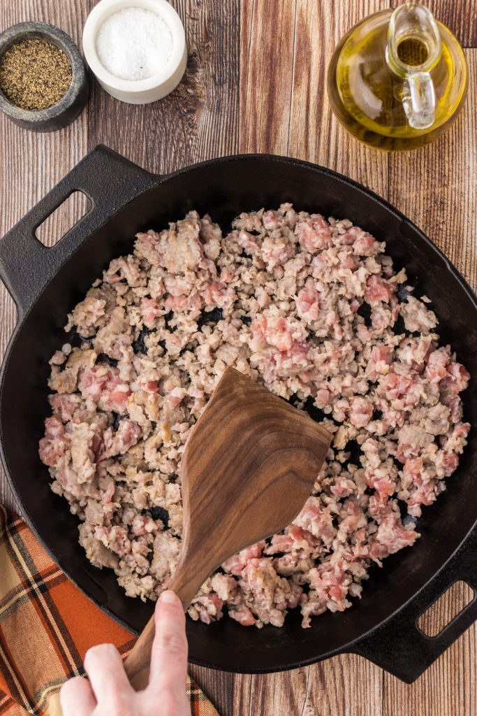 Use a wooden spatula to brown the sausage evenly in a large cast iron skillet.