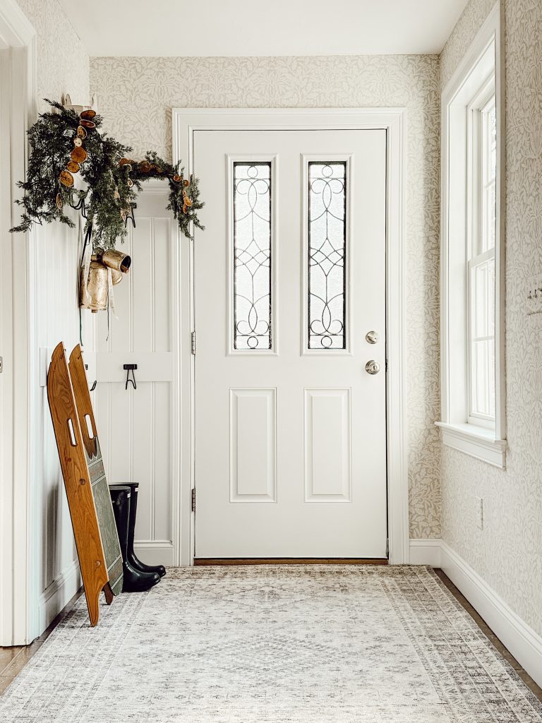 Vintage Christmas decorations in entryway with gold bells, vintage sleigh, and a dried fruit garland.