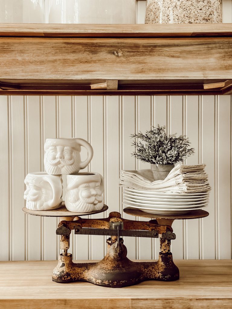 Holiday vignette with Santa mugs, a vintage scale, and holiday linens.