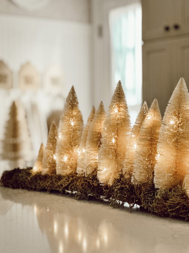 Cozy Christmas decor on kitchen island with bottle brush trees and festive Christmas lights.