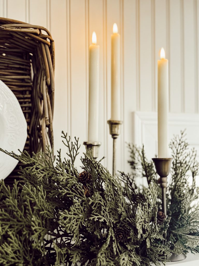 Flameless taper candles in candle holders on a shelf in the kitchen decorated for the holidays.