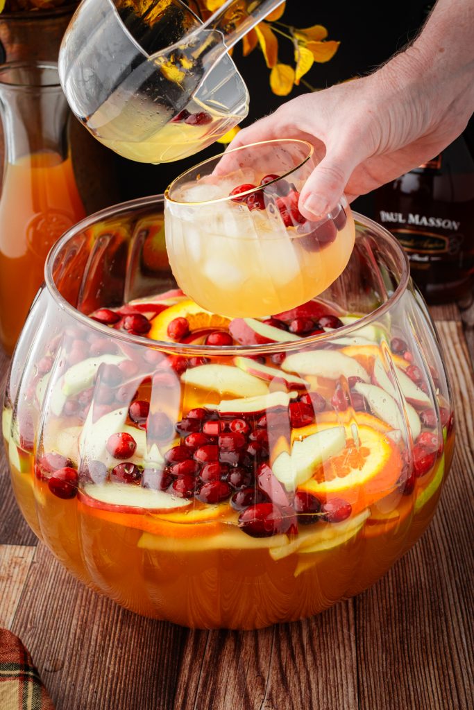 Glass full of fall sangria with fresh fruit, cranberries, cinnamon sticks, and star anise.