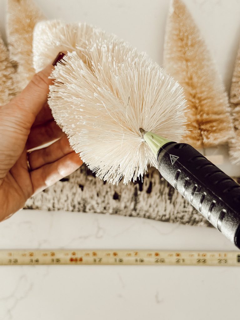 Apply hot glue to the bottom of the bottle brush tree to adhere it to the centerpiece base.