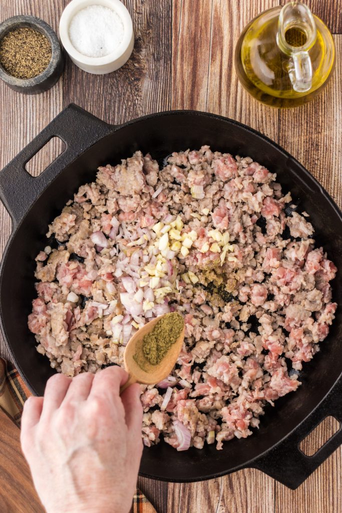 Sprinkling poultry seasoning on cooked sausage for the pumpkin filling.