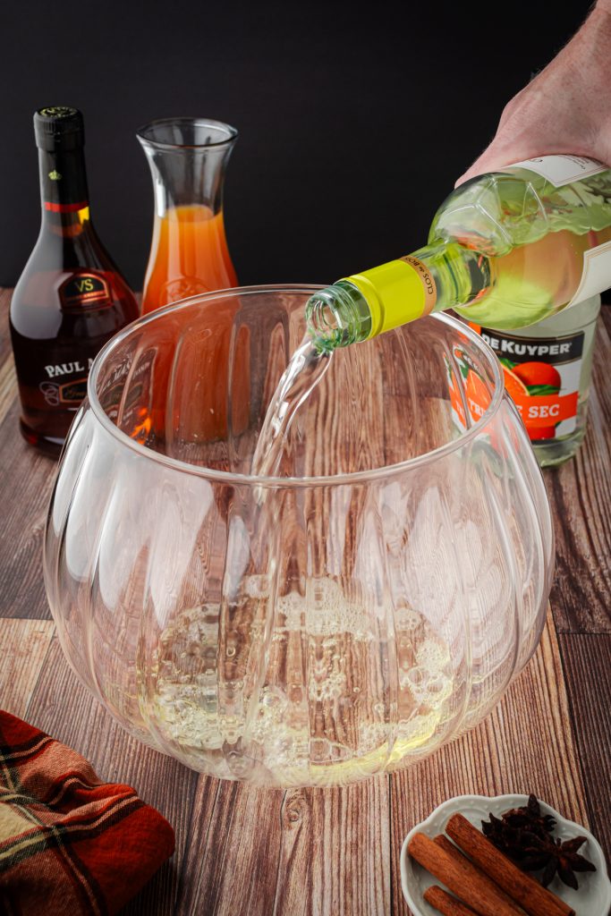 Add the dry white wine like a Pinot Grigio to a punch bowl to start the sangria.
