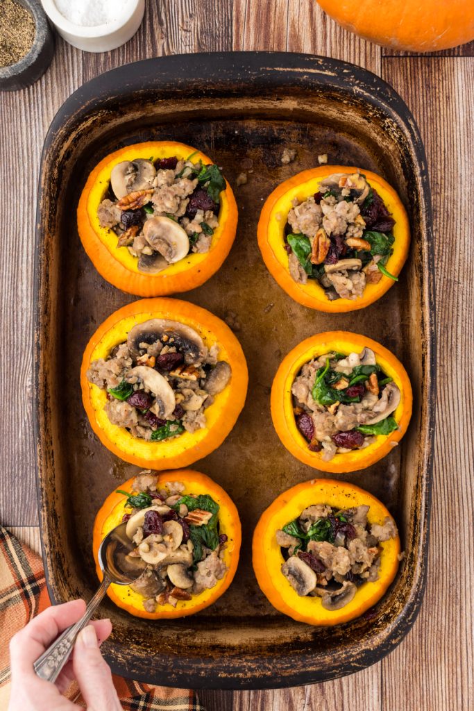 Spooning the stuffing mix into the roasted pumpkins for a cozy fall dinner.