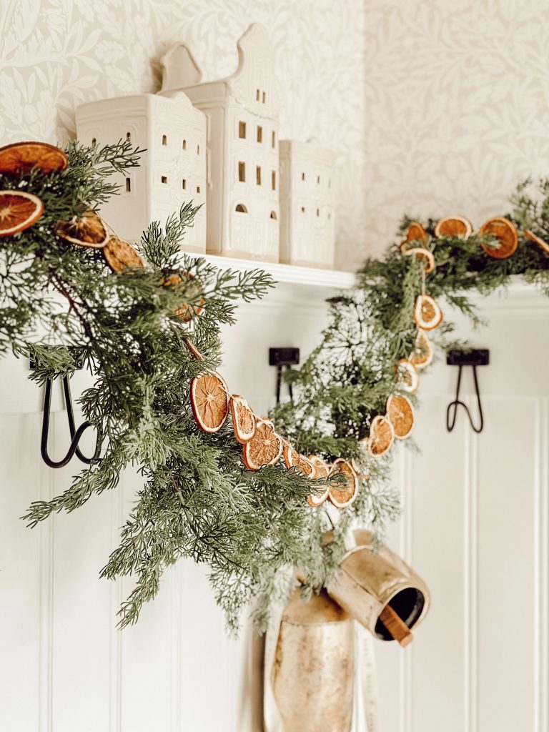 White ceramic houses with natural elements like fresh greenery and dried orange slices for the holiday season.