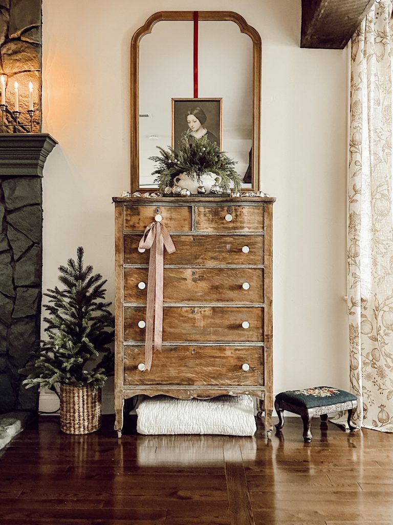 Dresser in living room decorated for the Christmas season with vintage artwork, natural greenery, and ornaments.