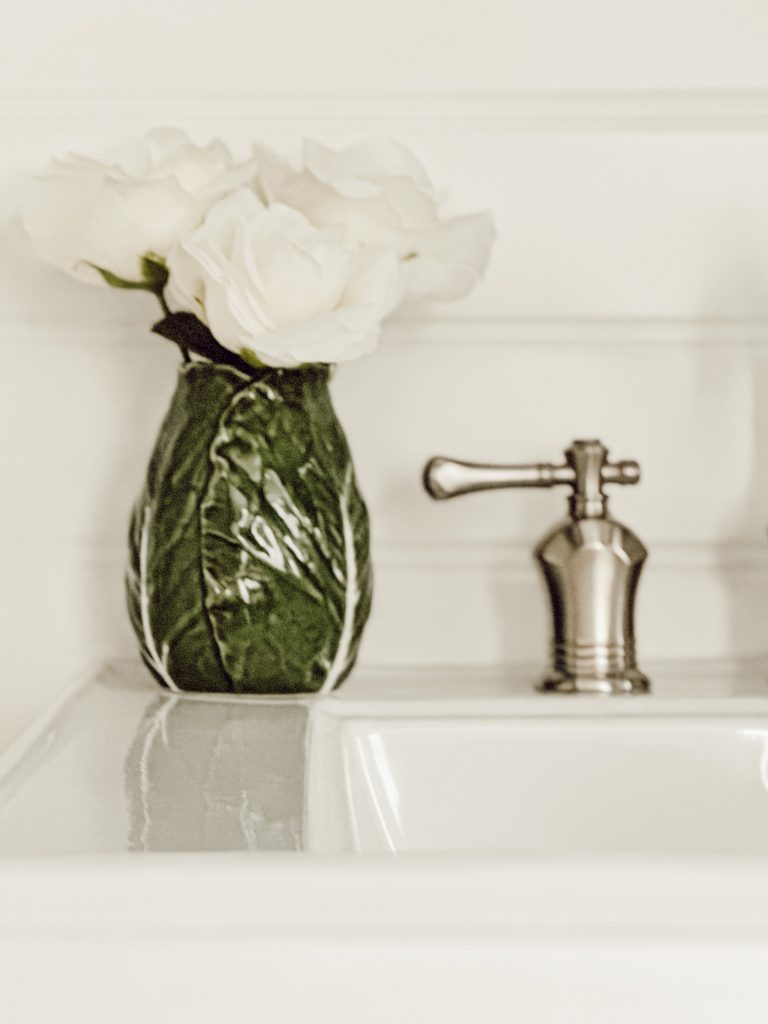 Cabbageware vase with white roses on bathroom sink counter. 