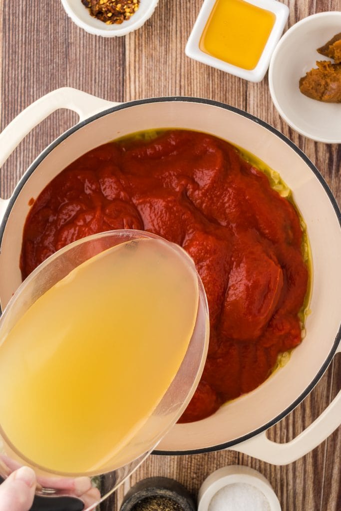 Chicken broth poured into tomatoes in a soup pot to create the base of the soup.