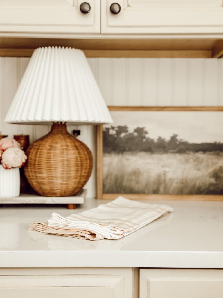 2025 spring home decor trends include natural elements like this rattan table lamp and milk glass vase with fresh flowers.